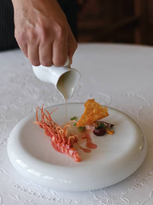 Chef pouring sauce over a prawn dish