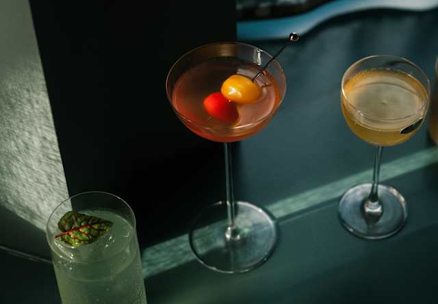 Three cocktails served in different styles of glassware on a dark surface.