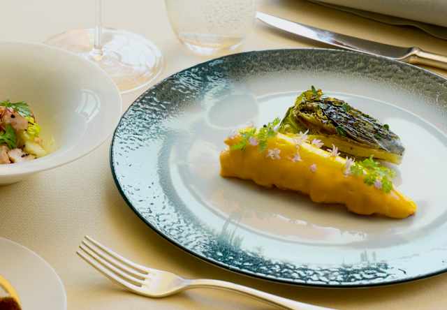 View of an Oro dish of a pasta parcel sprinkled with edible flowers and herbs, accompanied by grilled fennel and white wine.