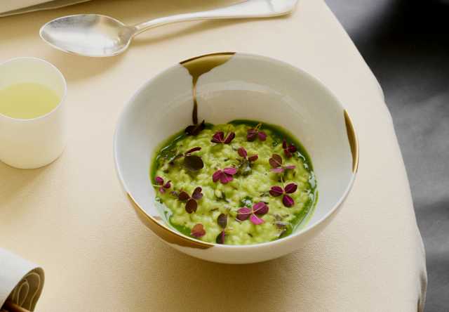 Looking down on a vibrant seaweed risotto with green tomato extract and sorrel, served in a white bowl with gold hints.