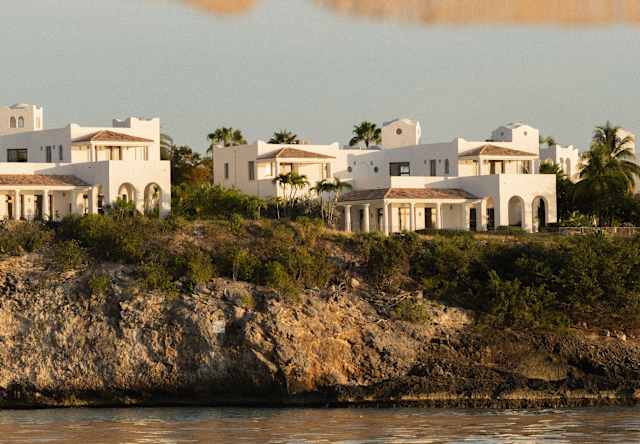White villas line the clifftops at the south end of Long Beach, seen from beneath the fringe of an orange and white parasol.