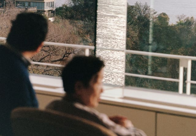 In soft-focus foreground, two men look gaze at Sagami Bay from their hotel window in Atami, photographed by Cecy Young.