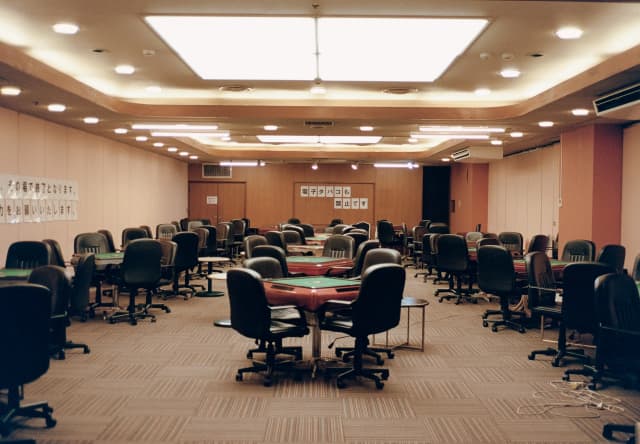 Ceiling spotlights illuminate a room with three rows of green-topped Mahjong tables in a hotel in Atami, taken by Cecy Young.