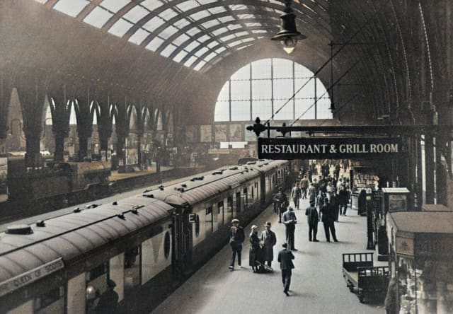 Historic photo of Kings Cross Station taken from above, capturing the Queen of Scots train, passengers and a restaurant sign.