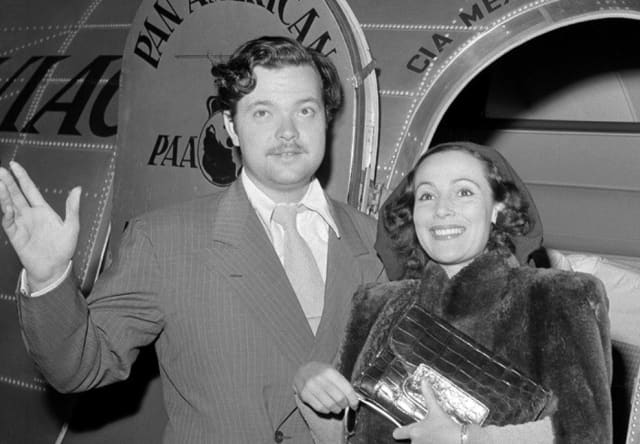 Black and white photo of American actor-director, Orson Welles and Mexican actress, Dolores del Rio, in an aeroplane doorway.
