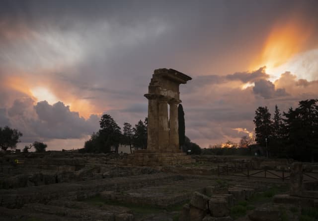 Jagged ruins at the Temple of Castor and Pollux in the Valley of Temples rise against a moody sky of sun and storm cloud.