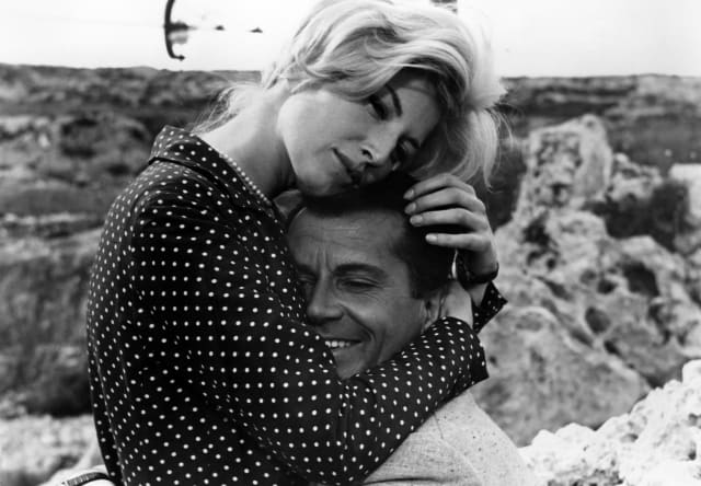 Monica Vitti, wearing a polka dot shirt, embraces Gabriele Ferzetti in a scene from the film L'Avventura, in black and white.