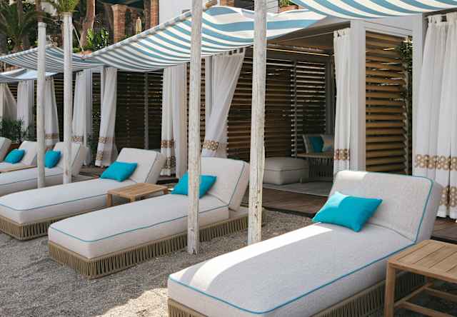 Five white loungers with blue cushions, shaded by canopies, offer perfect relaxation outside Lido Villeggiatura's cabanas.