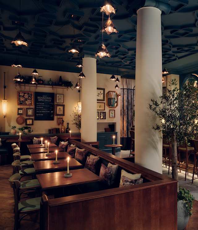 A stylish, dimly lit bar with a long marble counter, high-backed chairs, wooden tables with candles, framed art on the walls, and shelves of bottles behind the bar; cosy and elegant ambience.