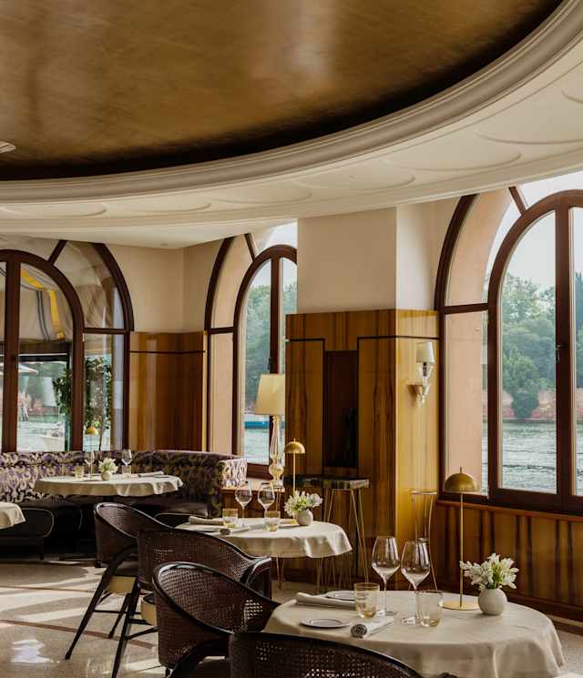 Three huge arched windows bring light and water views to round tables laid and awaiting guests in a view over Oro restaurant.