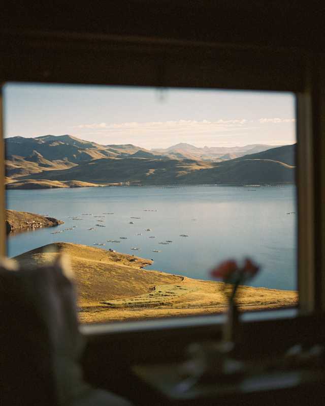 View of Lake Titicaca, surrounded by undulating hills, kissed by golden morning sun, seen through a cabin window.