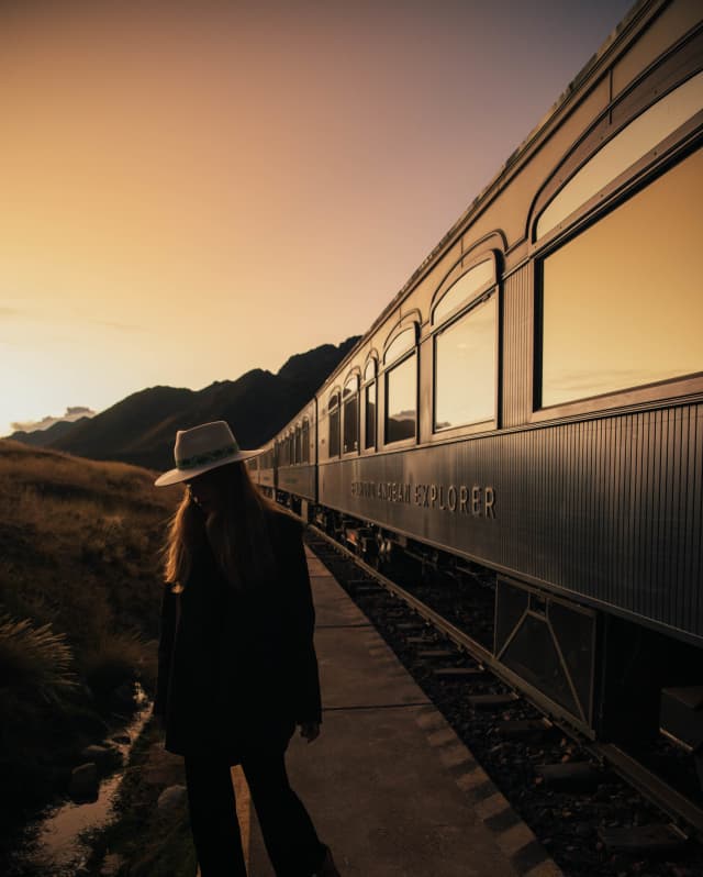 A woman with a fedora hat standing near the Andean Explorer at sunset