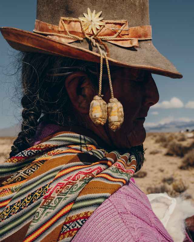 Profile image of a Uros woman in a brown felt and leather hat adorned with ribbon and pendants, and an intricate woven shawl.