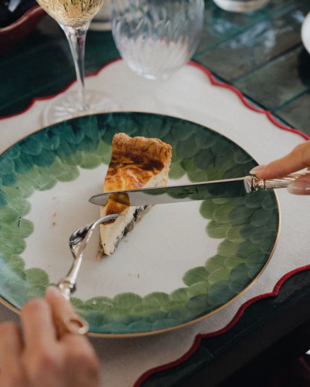 A guest cuts into a slice of quiche with a perfectly browned top and crisp pastry, on a green and white china plate.