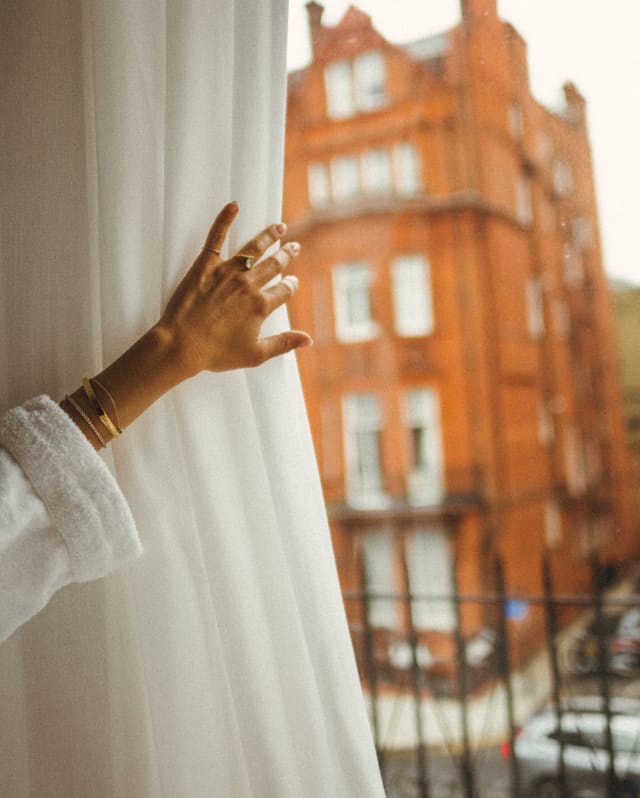 The hand of a female guest pulls back a curtain to reveal a view of the grand red-brick Victorian London townhouse opposite.
