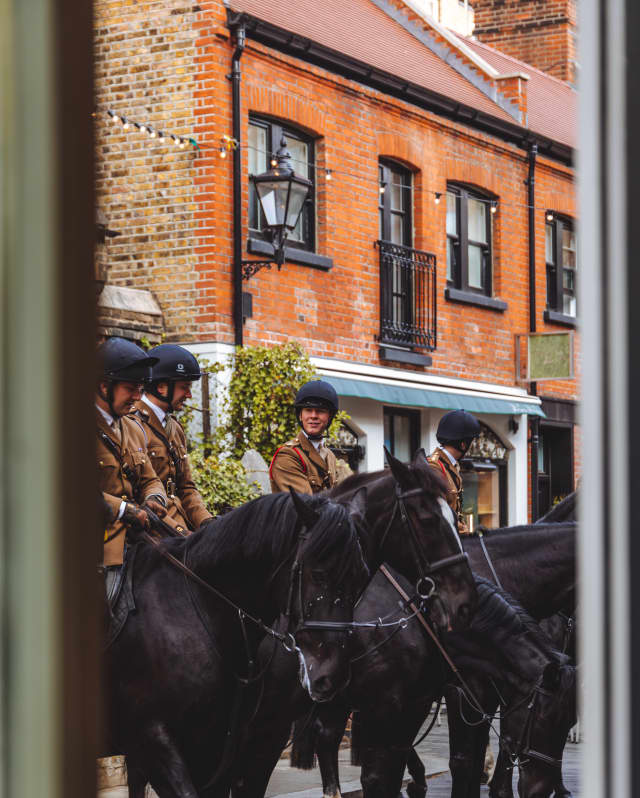 A glimpse through a window of four Household Cavalry Guards in khaki uniform and dark helmets mounted on black horses.