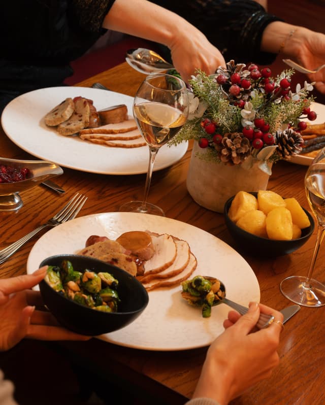 A guest spoons a helping of Brussel sprouts on to her plate of turkey and stuffing as her companion reaches for a side-dish.