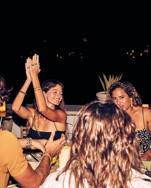 Smiling lady clapping her hands while conversing with guests in an open-air restaurant at night