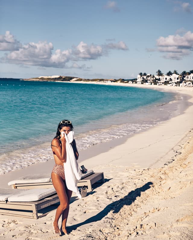 Lady holding a towel to dry her face on the curving shoreline of Maundays Bay