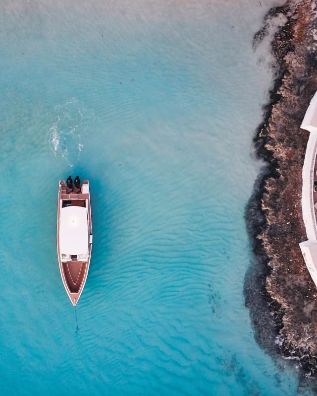 Birds-eye view of a lone ship sailing over cerulean water at sunset