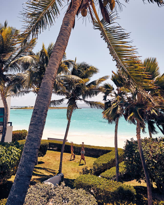 A couple doing hand stands in the manicured garden of a beach villa overlooking the Caribbean Sea