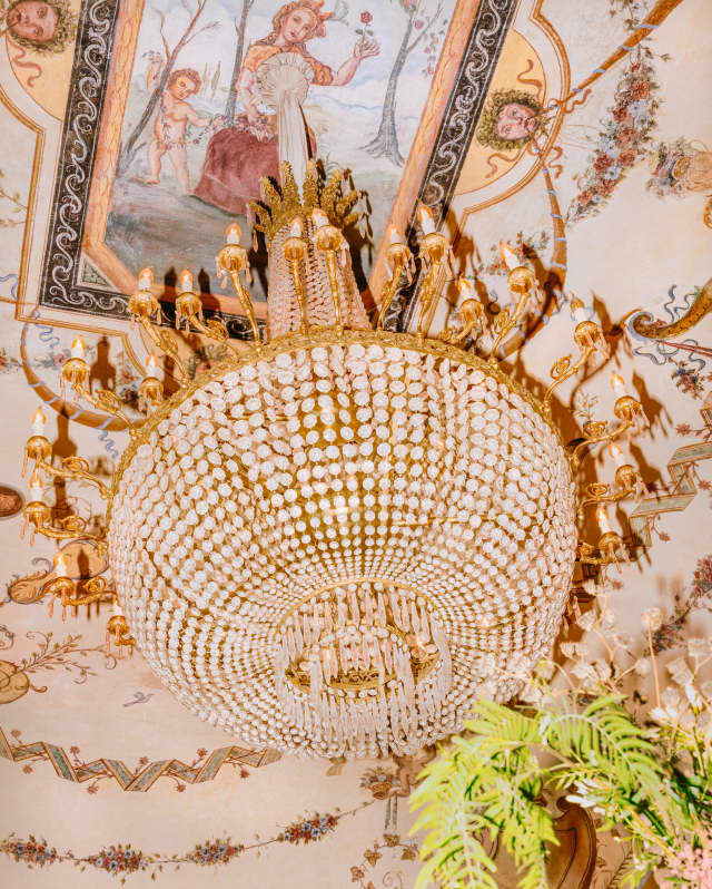 A large crystal chandelier hangs below an ornate and colourful fresco of flowers and mythical gods