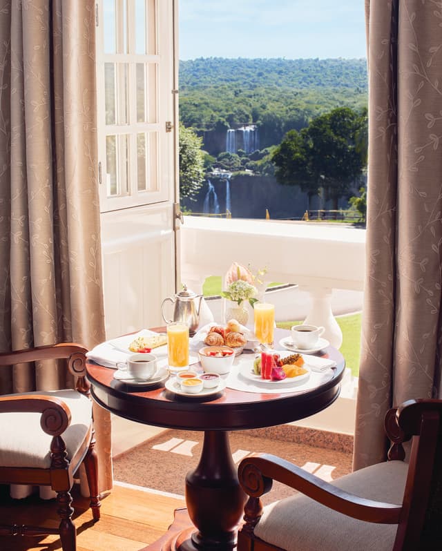 Circular table laden with breakfast dishes next to a sunny balcony