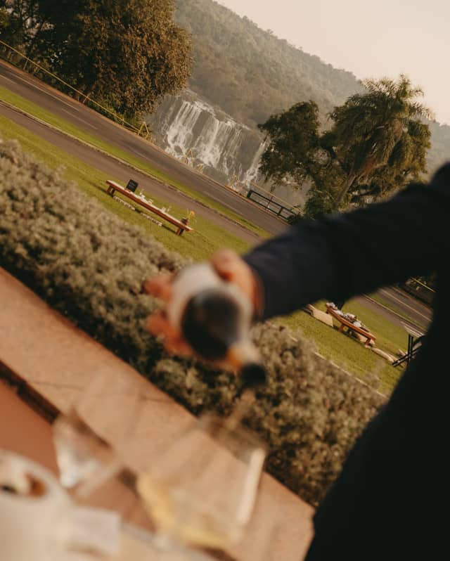 The hotel lawns reach towards the incredible cascading Iguassu Falls, while champagne is poured in soft-focus foreground.