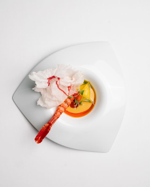 A stunning, delicate dish of Moqueca stew, with a grilled prawn tail and smoked tomato, served with a crisp, seen from above.