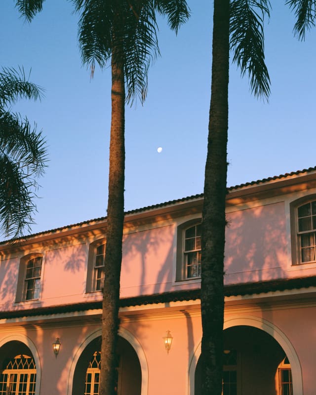 Tall palms spill shadows on the pink exterior of the hacienda-style Hotel Das Cataratas, glowing in rosy early evening light.