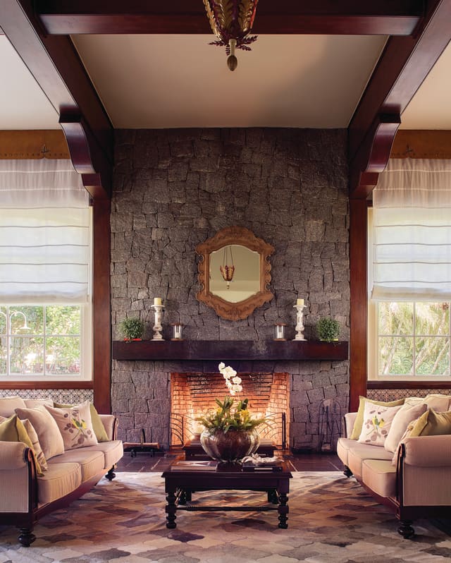 Two pale cream sofas and a coffee table before a fireplace on a stone wall