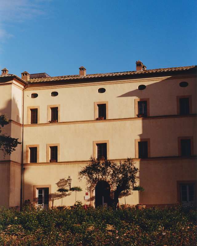View over gardens of the exterior of Casello di Casole with three levels of doors and windows in warm honey-toned walls.