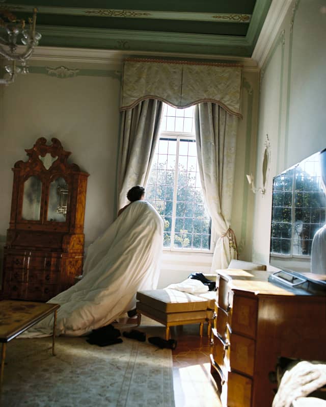 A guest, dragging a duvet, stands at a light-filled window in the Dogaressa Suite bedroom, gazing through the leaded panes.