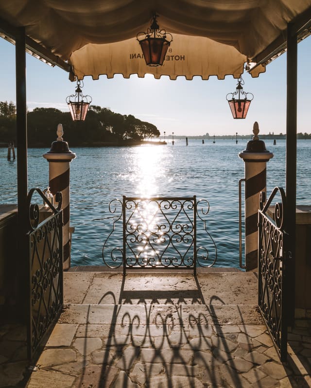 View of the glittering Venetian Lagoon along a stone pier with an awning and rose glass lanterns