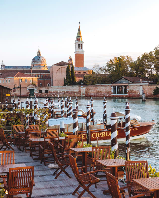 Wooden cafe tables on a terrace beside the Venetian Lagoon with views of St Mark's Square