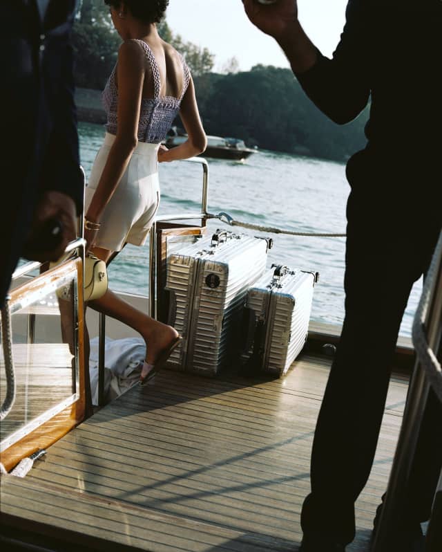 A woman in white shorts descends steps aboard a shuttle boat on the canal, leaving two silver-tone cases on deck.