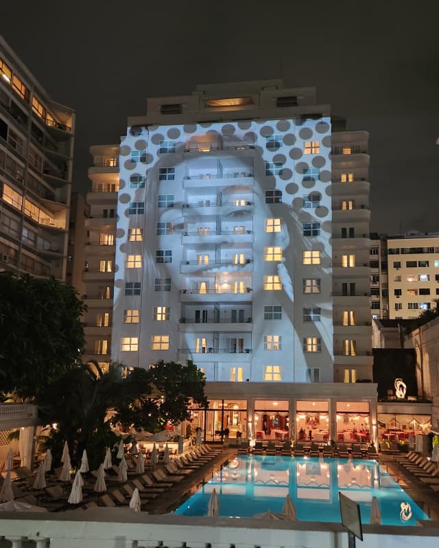 The face of a smiling woman is projected on the hotel façade at night, by artist JR and Casa Amarela for Mother's Day.