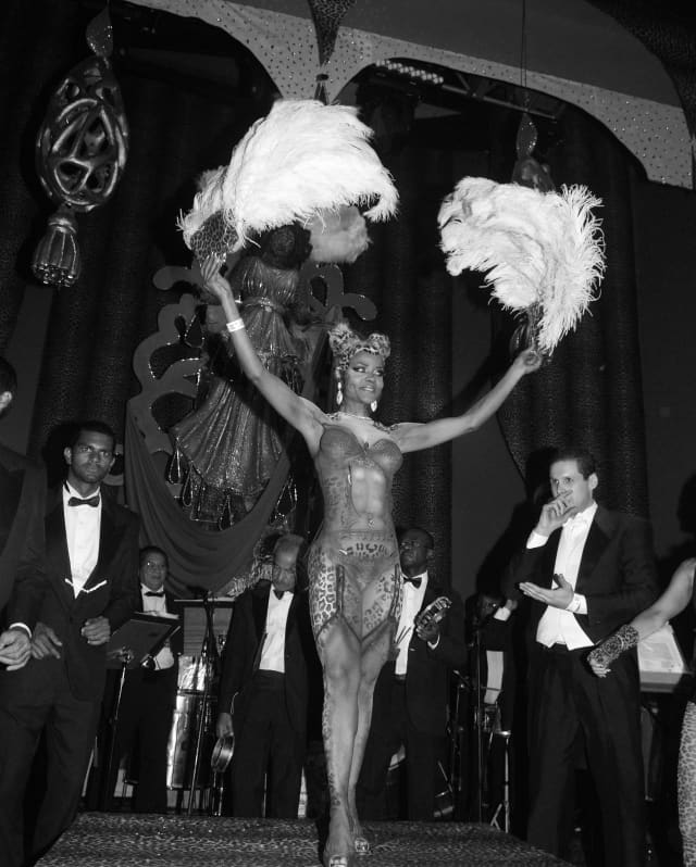 A samba dancer in carnival costume holds ostrich feathers aloft as she dancers to the rhythm of the live band behind her