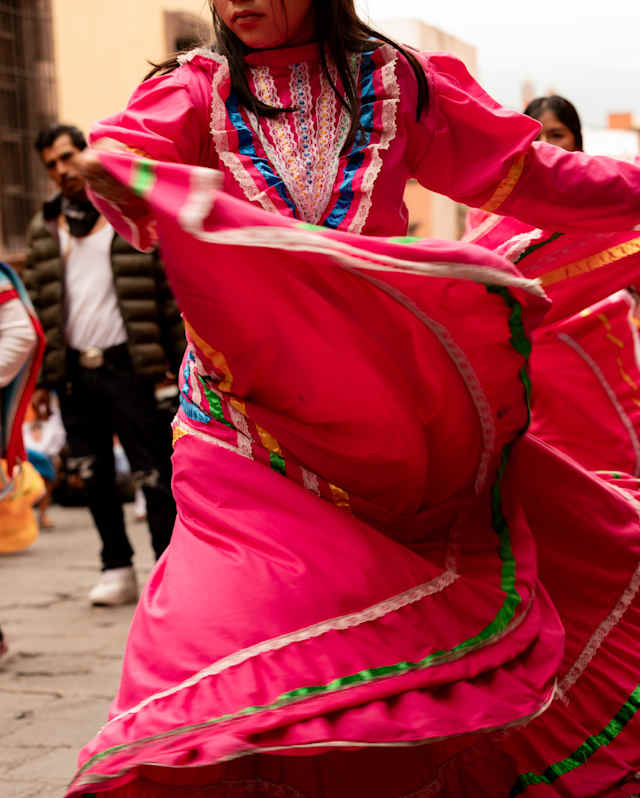 A woman swishes the wide skirt a red dress with green, white and blue embellishments as she dances to celebrate La Alborada.
