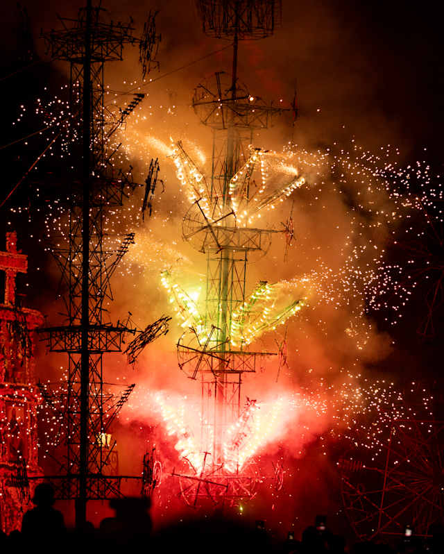 A tall structure with fireworks exploding in yellow, green and red is pictured against the night sky during La Alborada.