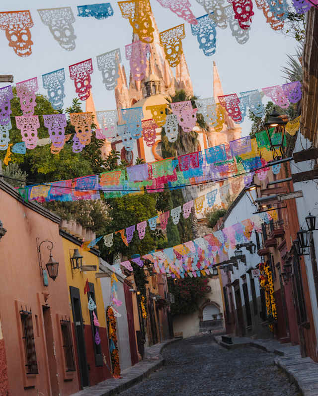 Angled image of the spires of Parroquia de San Miguel Arcángel rising behind a street fluttering with papel picado bunting.