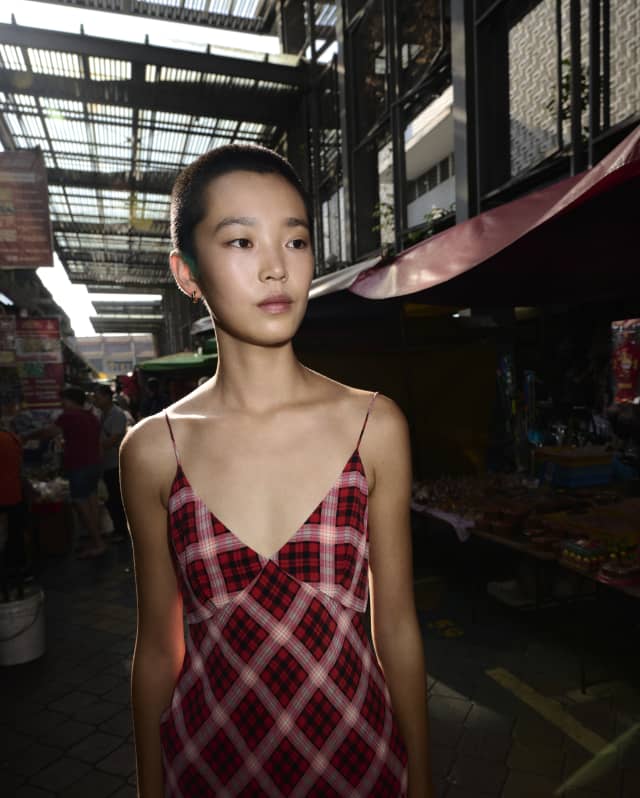 Kitajima photographs Balinese model, Echo with short dark hair, at a market wearing a strappy Marc Jacobs-style plaid dress.