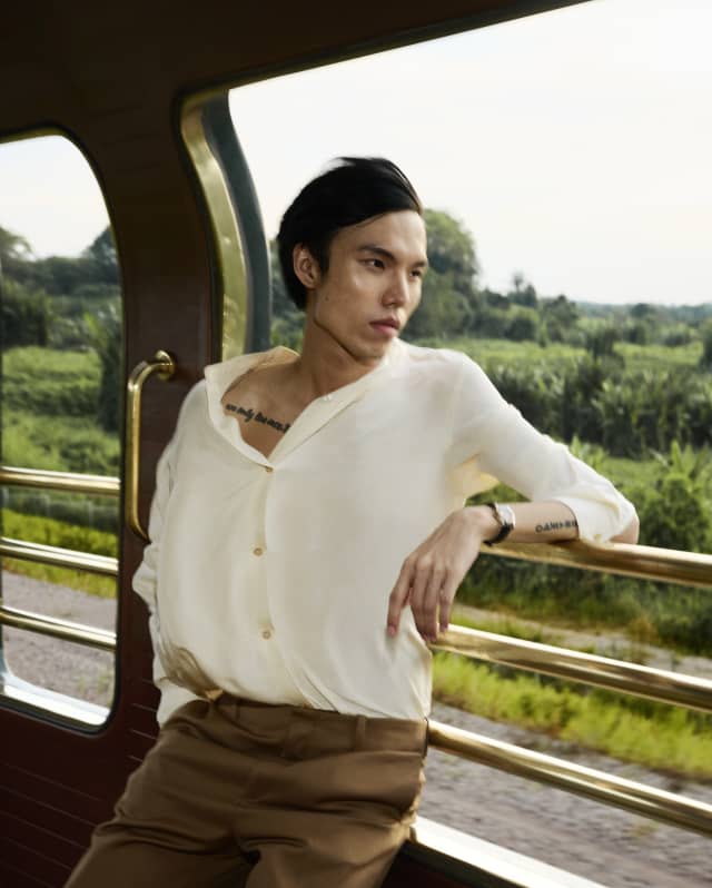 A man leans back on the side rails of the Observation Car, gazing down the tracks, with the wind in his hair and white shirt.