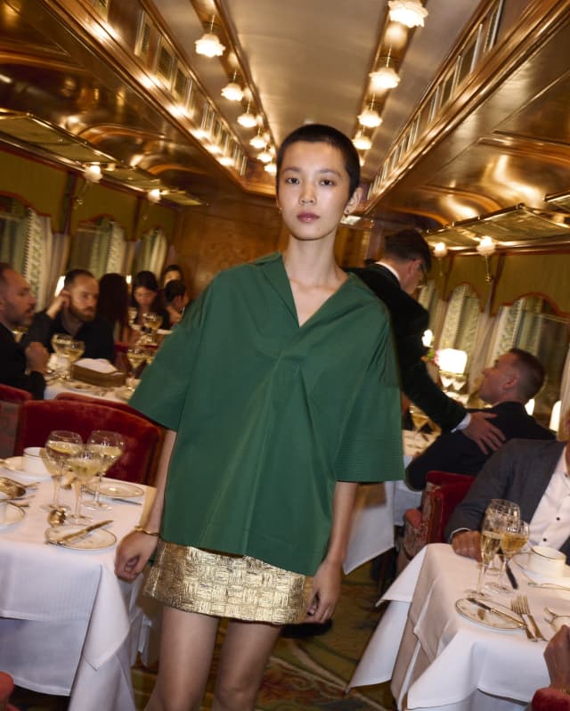 A model in a green top and gold miniskirt walks through the restaurant where every table is busy with guests, food and wine.