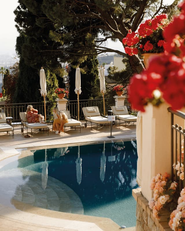 Guests reclining on sunbeds by a calm outdoor pool surrounded by Mediterranean gardens