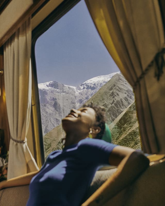 A female guest in a blue top basks in sunshine from the window behind her, which has views onto the incredible Andean peaks.