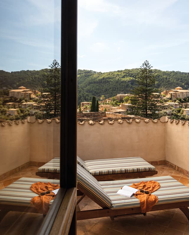 Teak sun loungers with striped cushions and a view over the hillside of Deià are reflected in the glass of an open window
