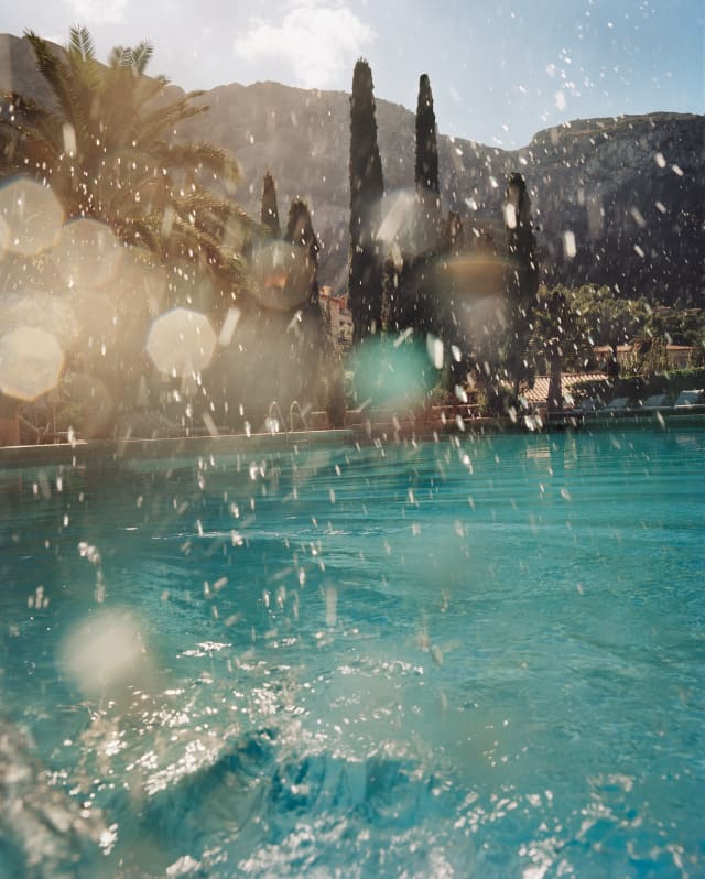 Sunlight glitters on tiny water droplets thrown into the air from a splash into a pool. Stone pines and palms reach for the sky
