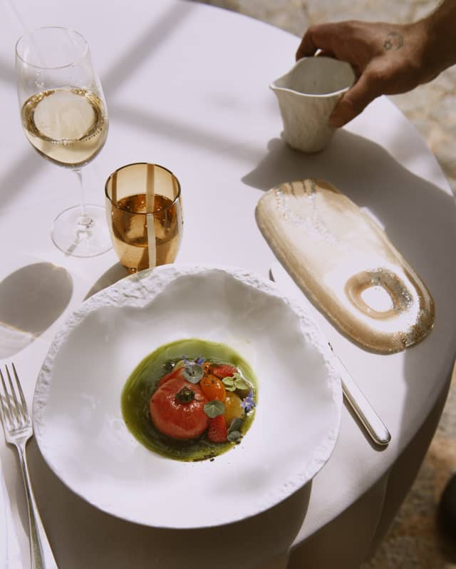 A vibrant vegan appetizer comprises a local Ramallet tomato in green tomato juice with grilled strawberries and black olive.
