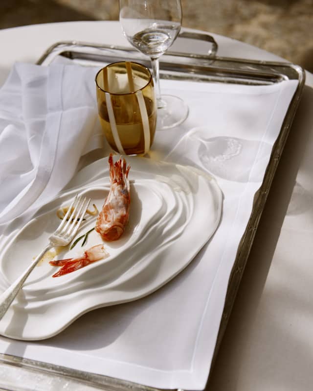 A half-finished dish of red prawns cooked in salt and served on an oyster shell-shaped plate rests on a cloth-covered tray.